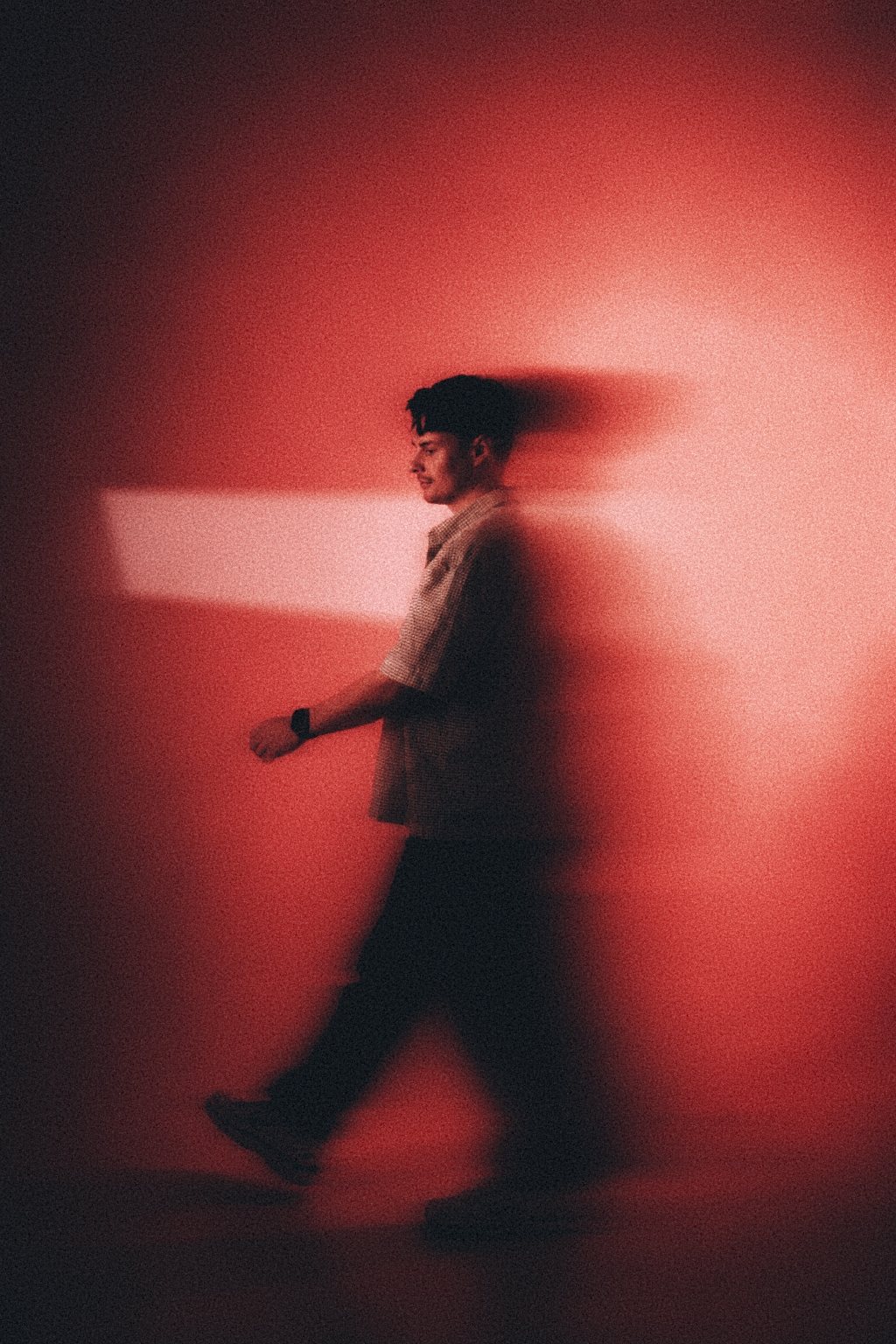 MOTIIV walking past a beam of light against a red backdrop
