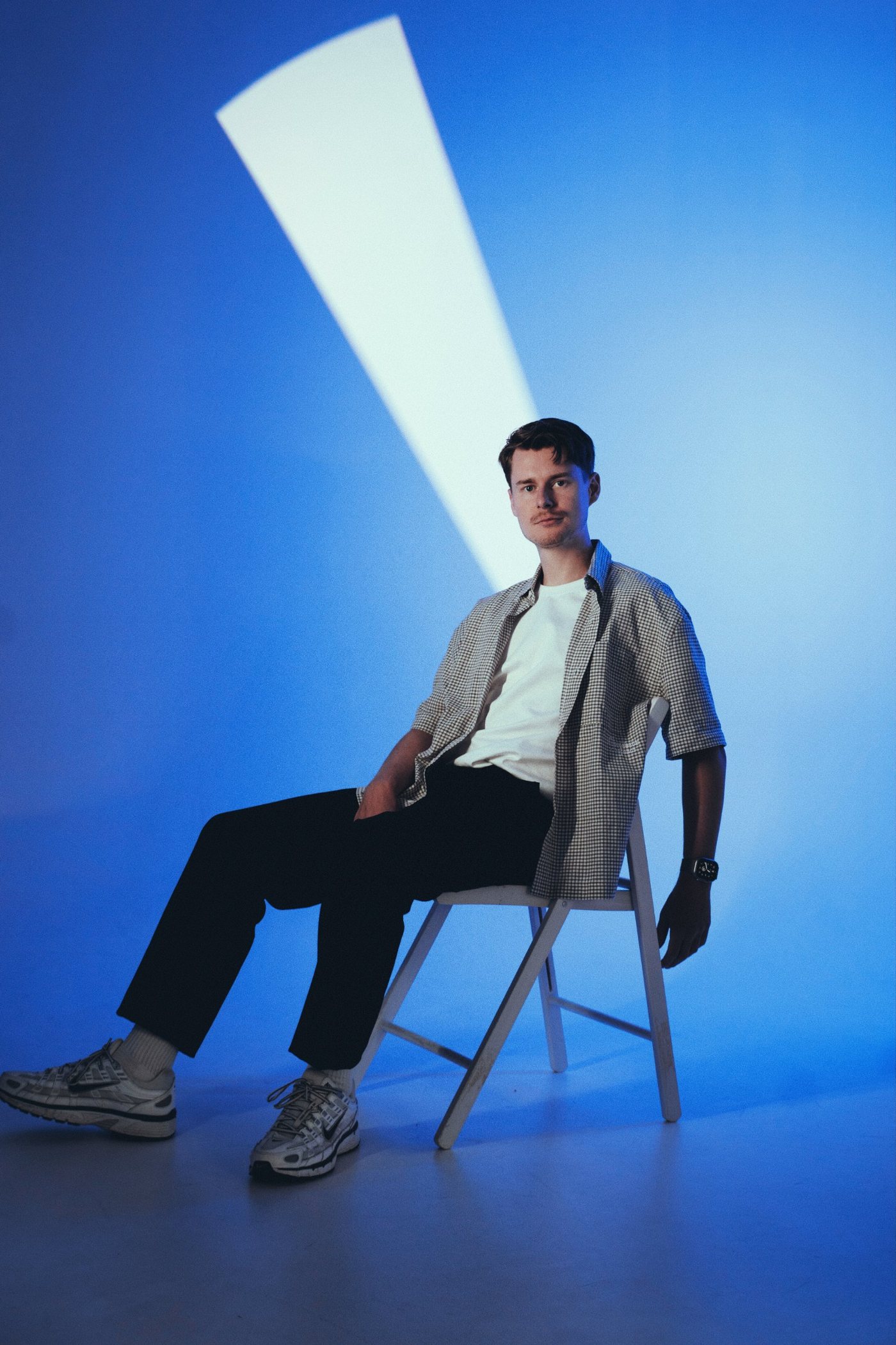 MOTIIV seated on a white chair under a beam of light against a blue backdrop
